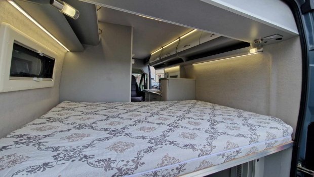 Wnętrze kampera z dużym łóżkiem, wzorzystym materacem i górnymi szafkami LED