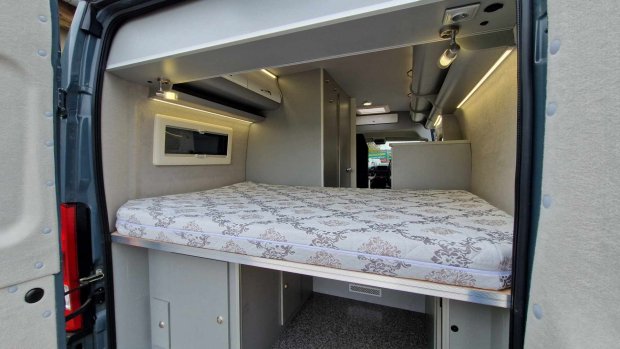 Wnętrze kampera z łóżkiem, szafkami i oświetleniem LED