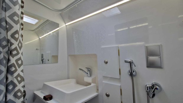 Mała biała łazienka z umywalką, chromowaną baterią, prysznicem i wzorzystą zasłoną.