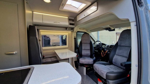 Wnętrze kampera z fotelem kierowcy, stołem jadalnym i zabudową kuchenną.