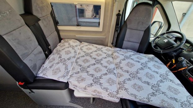 Złożone siedzenia tworzą łóżko w kamperze z jasną narzutą w wzory